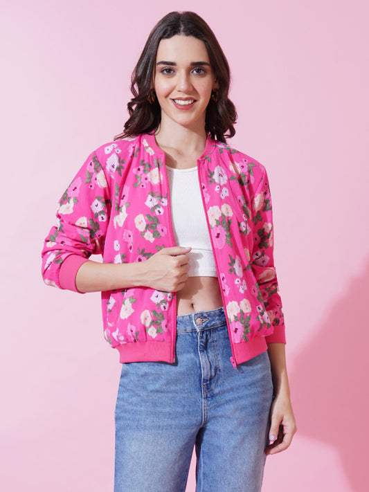 A woman wearing a pink and green leaf print bomber jacket with round neckline and long sleeves, paired with blue jeans.