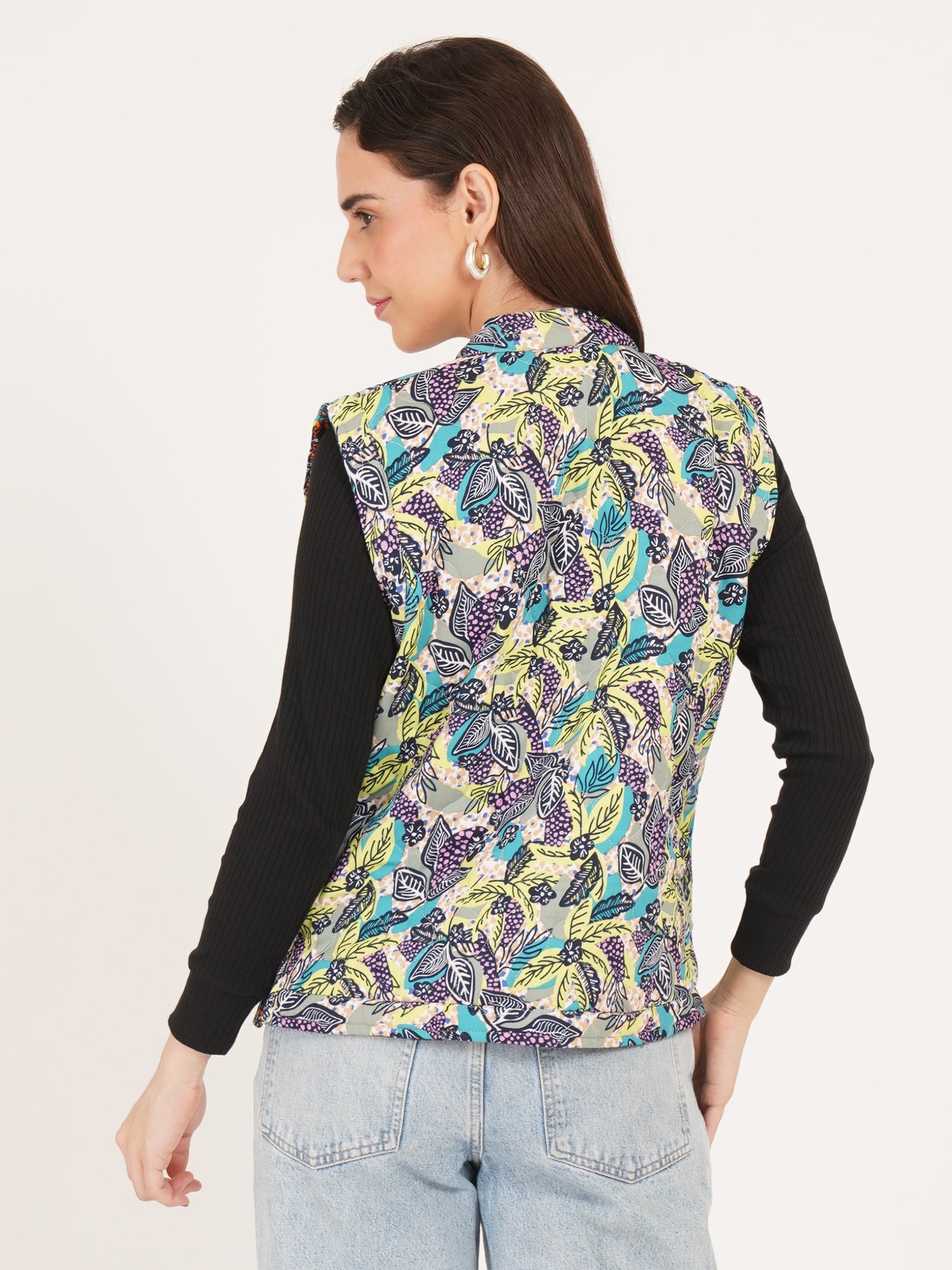 Woman wearing a colorful patterned vest over a black long-sleeve shirt on a light gray background