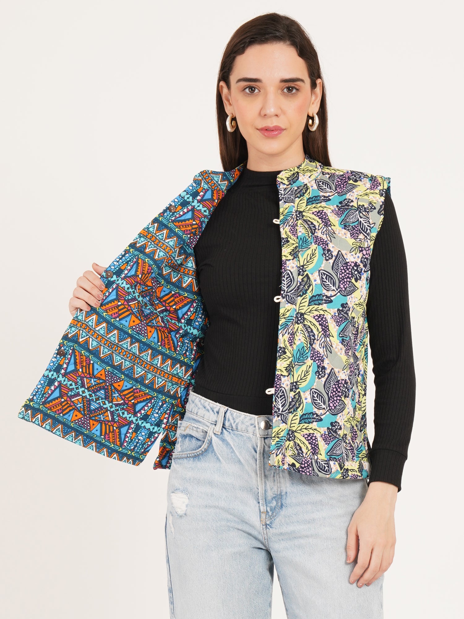 Woman reversible jacket wearing a colorful patterned vest over a black top and light blue jeans on a white background
