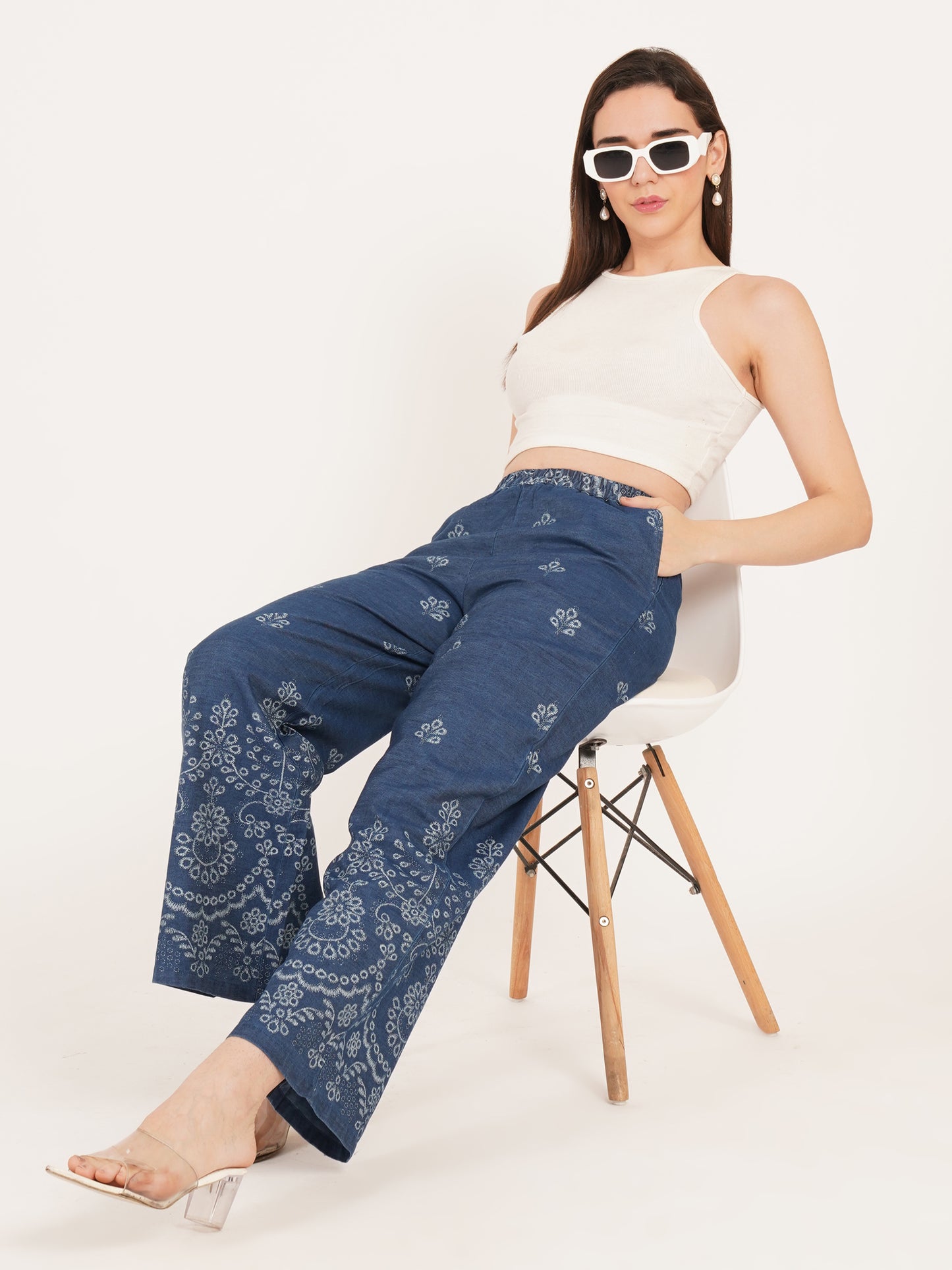 Woman wearing blue patterned pants and a white top sitting on a chair style a white background