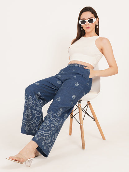 Woman wearing blue patterned pants and a white top sitting on a chair style a white background